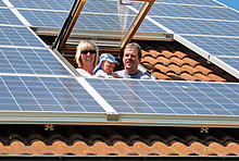 Solarmodule auf einem Dach mit Dachfenster, aus dem Frau, Baby und Mann herausschauen