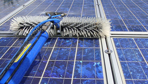 Solarmodule und Gerät zur Reinigung: Stiel mit Wasserschlauch und Stromkabel, vorne zwei Bürsten, mittig Spritzdüsen