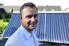 Portrait von Carsten Mönkemeyer vor einem Röhrenkollektor, im Hintergrund weitere Wohnhäuser
